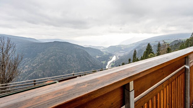 Une terrasse en bois donnant sur un paysage montagneux, avec une rivière.