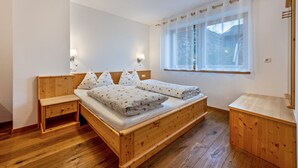 Un lit en bois, une table de chevet, une commode et une fenêtre ornée de rideaux légers.