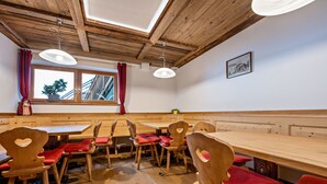 Un intérieur en bois avec une longue table et des chaises, une fenêtre avec des rideaux et un plafond avec des poutres en bois.