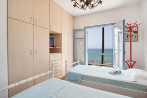 A bedroom with two beds, a wardrobe, and a balcony with a view of the sea.