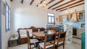A dining area with a wooden table and chairs, a chandelier, and a kitchen with wooden cabinets. - Vacation Home "On a Magnificent Sandy Beach" with Sea View, Terrace & Wi-Fi (Naxos)