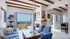 A spacious living room with a view of the sea, a chandelier, and a fireplace. - Vacation Home "On a Magnificent Sandy Beach" with Sea View, Terrace & Wi-Fi (Naxos)
