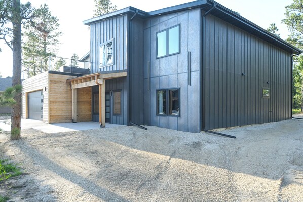 A modern two-story building with a garage, wooden deck, and large windows.