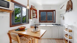 Una cocina con armarios blancos, una mesa de comedor de madera, una bombilla colgante y una ventana con vistas a la vegetación.