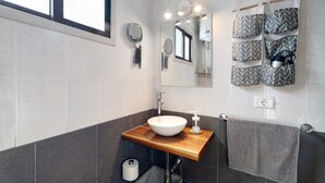 Un baño moderno con un tocador de madera, un espejo grande, un perchero con toallas estampadas y un dispensador de papel higiénico.
