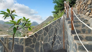 A stone staircase with a rope handrail, a potted plant, and a view of a mountainous landscape. - Holiday Home "Tajaraste 2" with Sea & Mountain Views, Private Terraces & Wi-Fi (Hermigua)