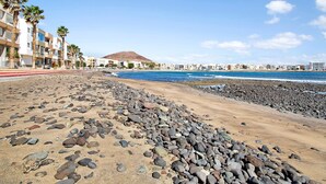 A beach with pebbles, a clear sky, and buildings in the background. - Vacation Apartment 'Ocean Side Arinaga' with Sea View and Wi-Fi (Arinaga)