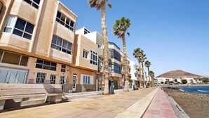 A coastal building with balconies, palm trees, and a beach view. - Vacation Apartment 'Ocean Side Arinaga' with Sea View and Wi-Fi (Arinaga)