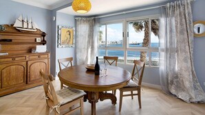 A dining area with a wooden table, chairs, a ship model, and a view of the sea through large windows. - Vacation Apartment 'Ocean Side Arinaga' with Sea View and Wi-Fi (Arinaga)
