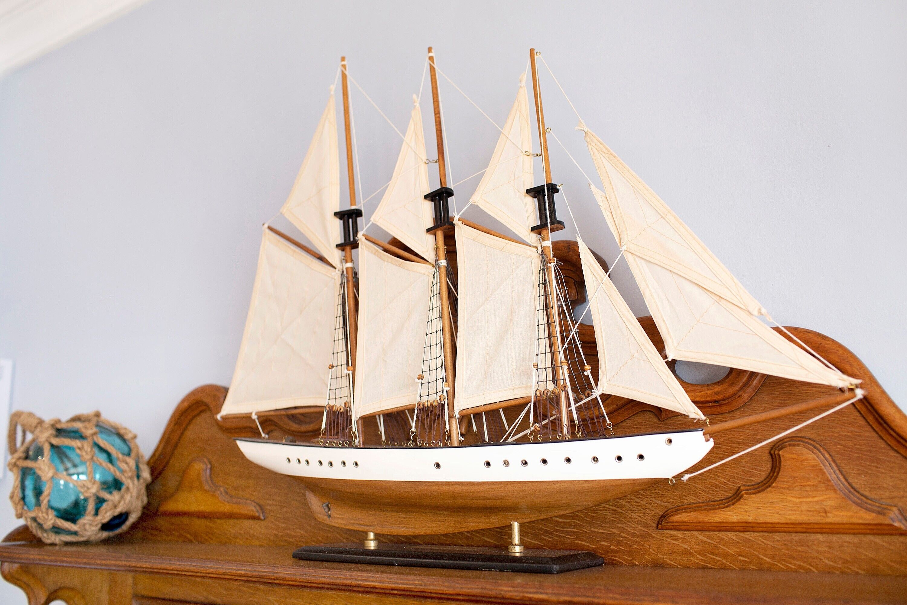 A wooden ship model with multiple sails, displayed on a wooden stand.