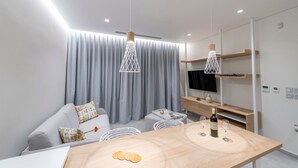 A modern living room with a sofa, a dining table, a TV, and a wooden shelf. - Villa "Suite Erifilli" with Sea View, Private Pool & Wi-Fi (Meganisi)