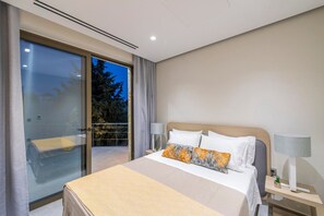 A modern hotel room with a large bed, a desk with a lamp, and a sliding glass door leading to a balcony. - Villa "Suite Erifilli" with Sea View, Private Pool & Wi-Fi (Meganisi)