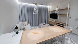 A modern living room with a dining table, sofa, and TV. - Villa "Suite Erifilli" with Sea View, Private Pool & Wi-Fi (Meganisi)