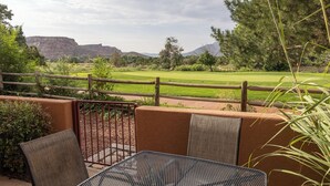 Een terras met een tafel en stoelen, met uitzicht op een golfbaan en bergen.