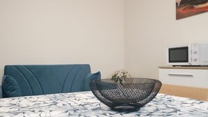 Una mesa de comedor con mantel estampado, un cuenco tejido negro, un sofá azul y un microondas sobre un mueble blanco.