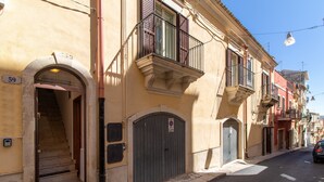 Una calle con edificios, un portón metálico cerrado y un coche estacionado al costado.