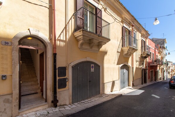 Une rue bordée d’immeubles, une grille métallique fermée et une voiture garée sur le bord.