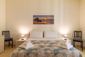 Une chambre d’hôtel avec un lit, deux tables de chevet, deux chaises, un tableau représentant un coucher de soleil et un lit soigneusement fait avec des serviettes.