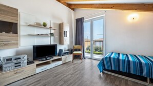 Et moderne værelse med et fladskærms-tv, træmøbler, en seng med stribet sengetøj og en balkon med udsigt.