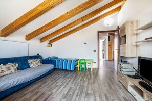 A room with a blue sofa, wooden beams, a TV, and a small table.