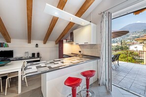 A modern kitchen with a central island, a dining area with a table and chairs, and a balcony with a view of the surrounding area.