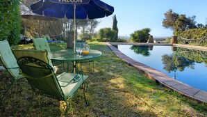 A poolside area with a table and chairs, a blue umbrella labeled 'FALCON,' and a view of the water. - Vacation Home "Arcadia T3" with Private Pool, 2 Terraces & Wi-Fi (São Bartolomeu de Messines)