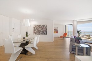 A modern interior with a glass dining table, white chairs, a sofa, and a view of the beach. - Apartment "Mare Nostrum" with Sea View, Shared Pool and Wi-Fi (Olhão)