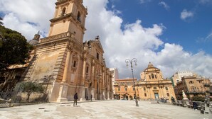 Un edificio histórico con una torre destacada, una cúpula y un patio con bancos.