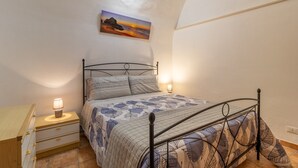 Un dormitorio con cama, lámparas de noche, mesita de noche, cómoda y un cuadro en la pared.