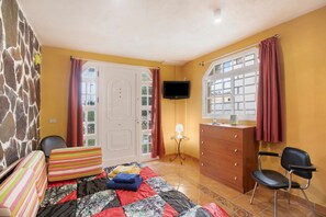 Une chambre à coucher comprenant un lit, une commode, une chaise, un téléviseur et une fenêtre avec des rideaux.