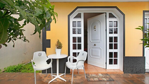 Een terras met twee witte plastic stoelen en een kleine ronde tafel, een deur met ruitpanelen en een welkomstmat op de vloer.