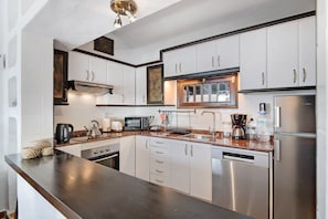 A modern kitchen with stainless steel appliances, white cabinetry, and a dark countertop.
