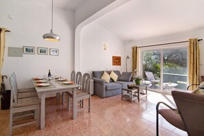 Un coin repas avec une table dressée pour quatre personnes, un canapé gris et un balcon avec vue.