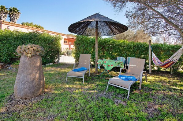 Un jardin avec un hamac, deux chaises et une table placés sous un grand parasol.