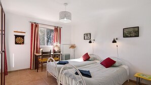 Ett sovrum med två sängar, ett skrivbord, en stol, en lampa och ett fönster med gardiner.