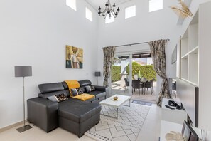 A modern living room with a sectional sofa, a coffee table, and a dining area with outdoor seating.