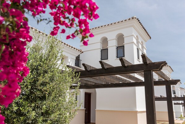 A white building with arched windows and a wooden pergola.