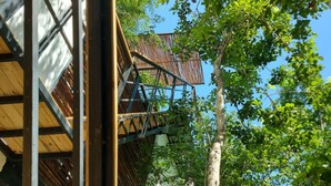 A wooden balcony with a metal railing overlooking a lush green area with trees. - Increíble Townhouse con piscina privada (Tulum)