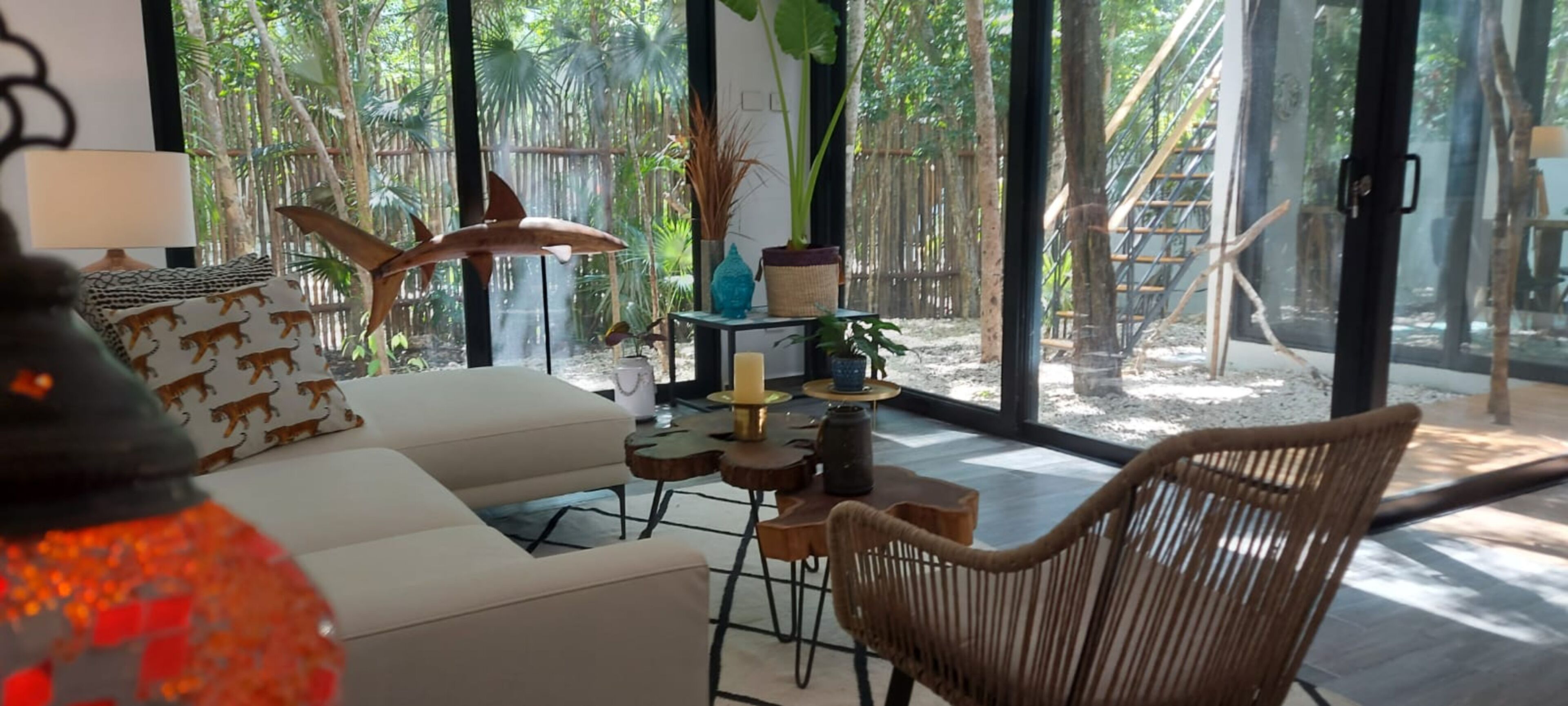 A modern living room with a white sofa, a wicker chair, a small table with candles, and a decorative shark sculpture.