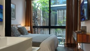 A modern bedroom with a large bed, a bathtub, and a view of greenery through a window. - Increíble Townhouse con piscina privada (Tulum)