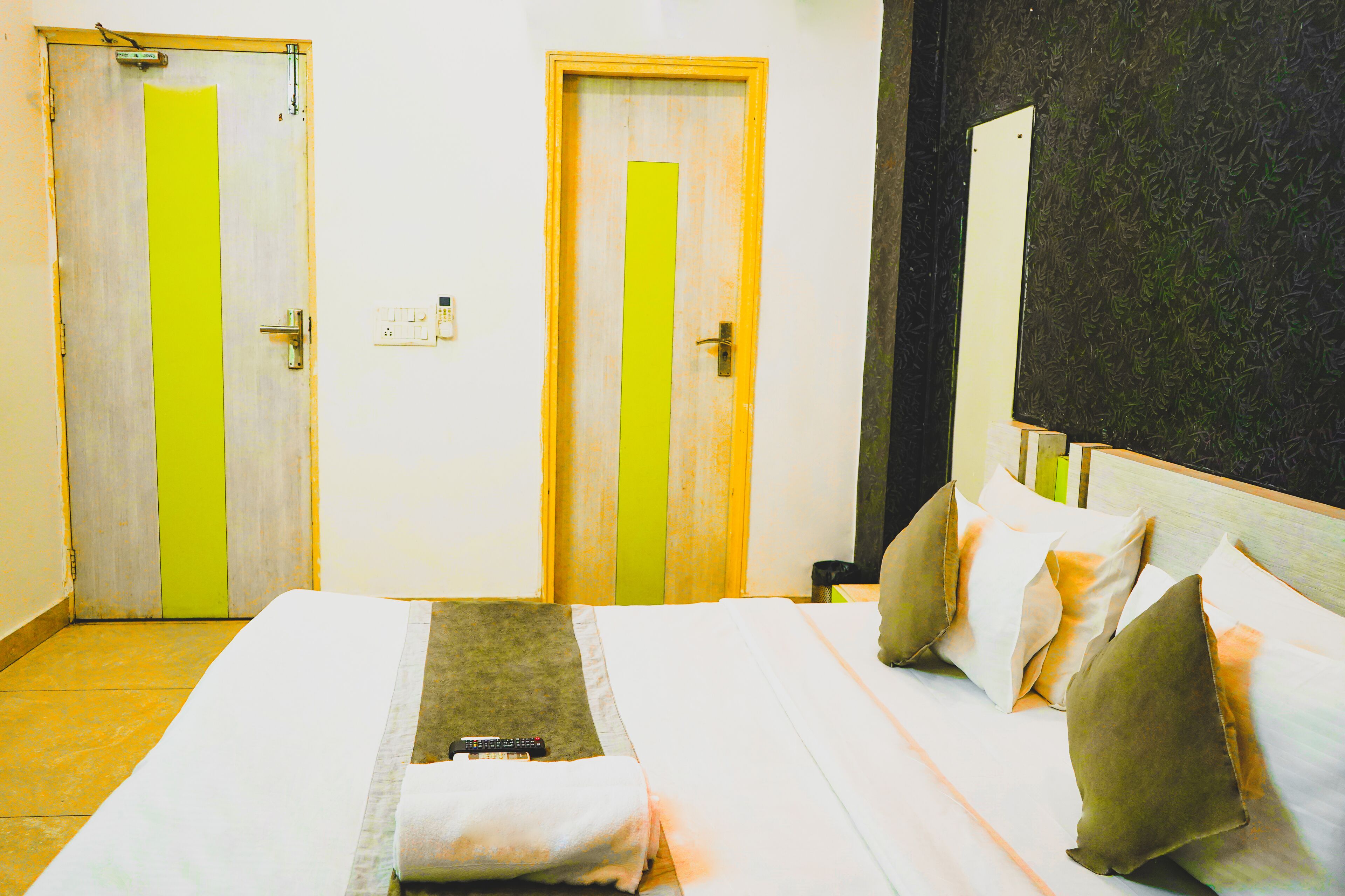 Una camera d'albergo con due porte, un letto con cuscini, un telecomando e un piccolo tappeto.