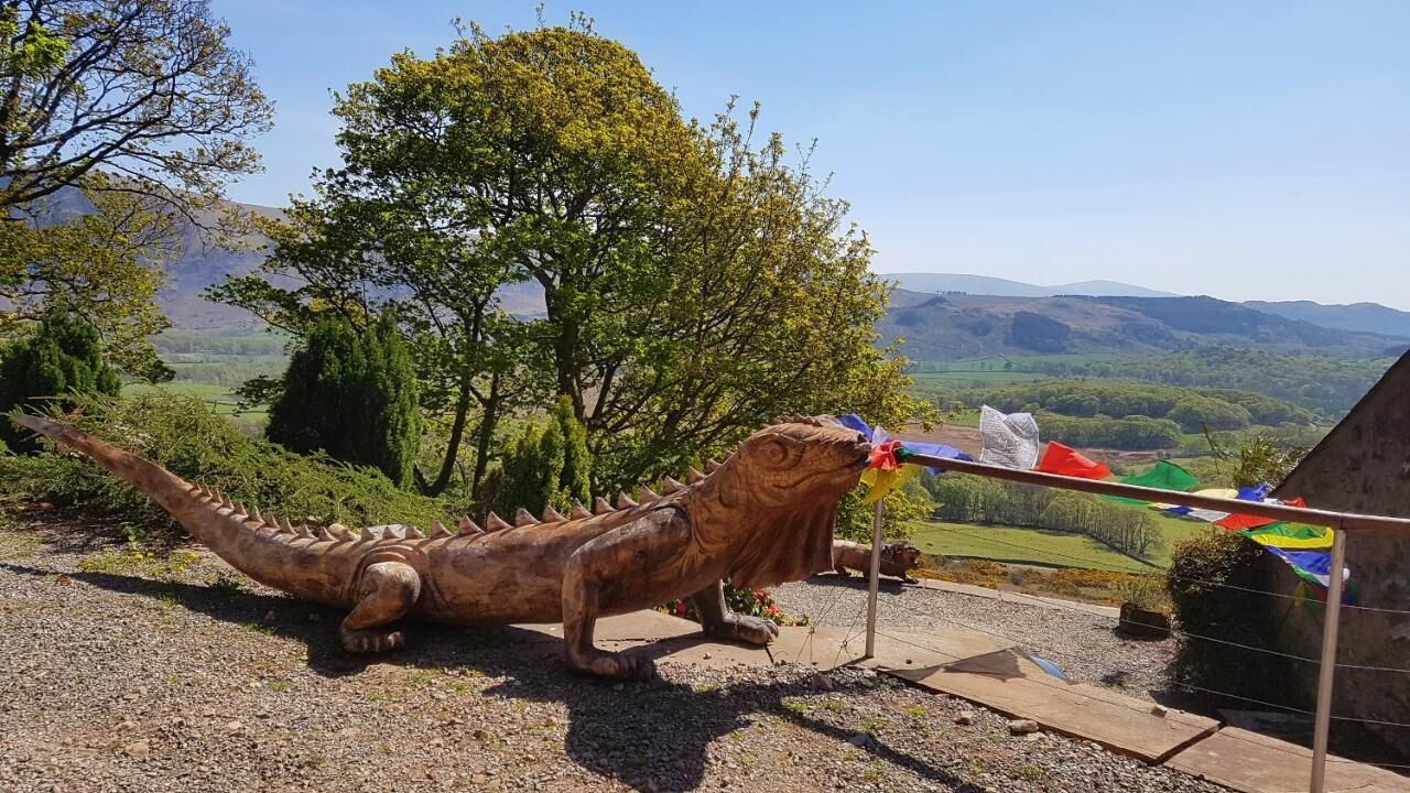 Escultura de dinossauro ao ar livre, com vista para um vale e montanhas ao fundo.