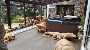 A covered patio with wooden furniture, a hot tub, and decorative animal sculptures. - Windsor Farm House , Stunning views/hot tub close to Scafell and Wastwater Lake (Wasdale)