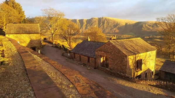 A rural village with stone buildings, a dirt road, and a mountainous backdrop. - Windsor Farm House , Stunning views/hot tub close to Scafell and Wastwater Lake (Wasdale)