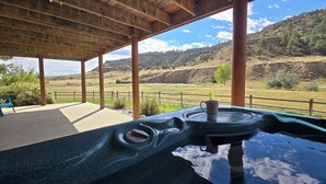 A covered outdoor area with a stone table, a wooden pergola, and a view of a hilly landscape. - Sky Creek Ranch Montana  Lodge House
 (Molt)