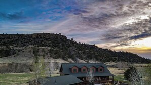 A log cabin with a garage and a covered porch, surrounded by a well-maintained lawn and a gravel driveway. - Sky Creek Ranch Montana  Lodge House
 (Molt)
