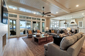 A spacious living room with a large sofa, coffee table, and a view of the beach through the sliding glass doors.