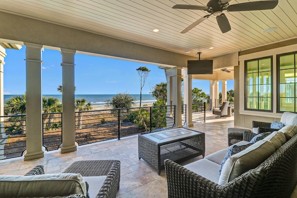 A covered outdoor patio with wicker furniture, a ceiling fan, and a view of the beach.