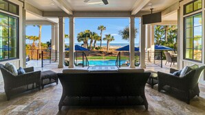 A covered outdoor seating area with wicker furniture, a pool, and a view of the beach and ocean. - New Oceanfront Oasis in Palmetto Dunes with a private pool and EV plug (Hilton Head Island)