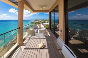 A balcony with a view of the ocean, wooden furniture, and a ceiling fan.